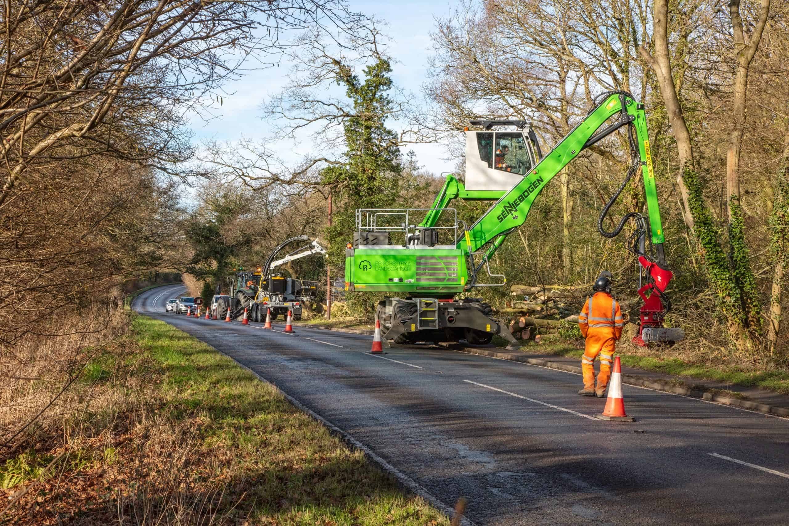 A Sennebogen machine dismantling roadside ash under a lane closure